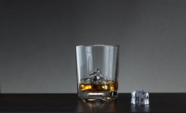 Tahta masadaki buzlu bir bardak viski. Bir bardak viski ve masanın üzerinde bir parça buz..