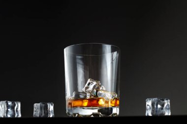 Karanlık bir arka planda buzlu bir bardak viski. Bir bardak viski ve masanın üzerinde buz.
