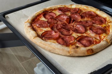 freshly baked pepperoni pizza on a baking sheet. Pizza taken out of the oven