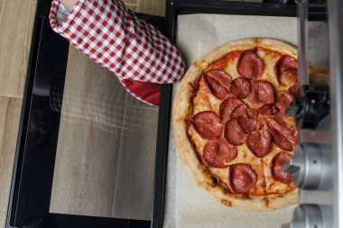 Kız pizzayı fırından çıkarıyor. Ev yapımı pepperoni pizza.