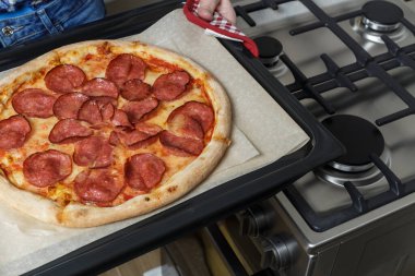 Kız pizzayı fırından çıkarıyor. Ev yapımı pepperoni pizza.