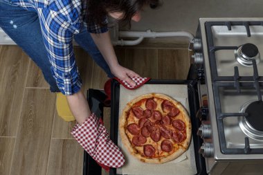 the girl takes the pizza out of the oven. homemade pepperoni pizza