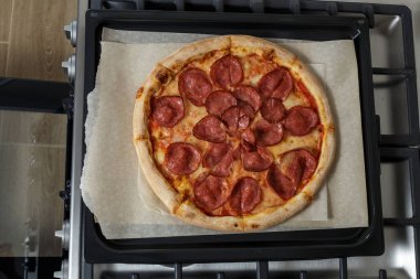 freshly baked pizza on a baking sheet and baking paper. a baking sheet with pizza is on the stove