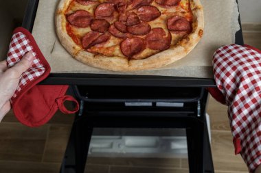 the girl takes the pizza out of the oven. homemade pepperoni pizza