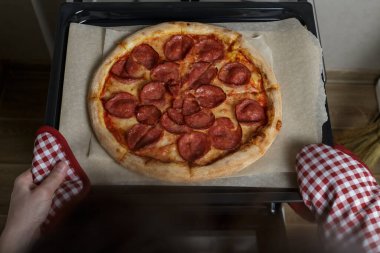 Kız pizzayı fırından çıkarıyor. Ev yapımı pepperoni pizza.