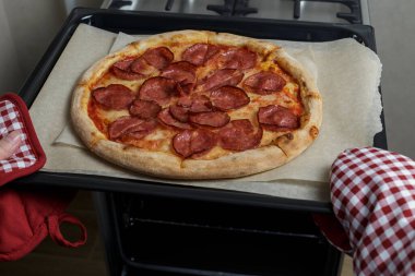 Kız pizzayı fırından çıkarıyor. Ev yapımı pepperoni pizza.