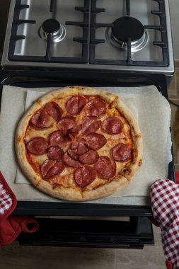 Kız pizzayı fırından çıkarıyor. Ev yapımı pepperoni pizza.