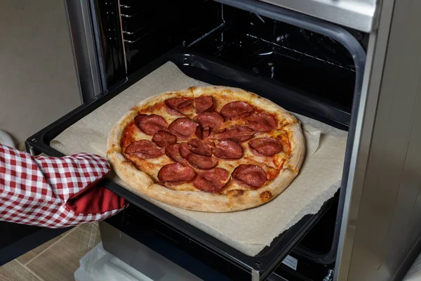 Pepperoni pizzası fırında fırında pişiyor. Şef pizzayı fırından çıkarır.