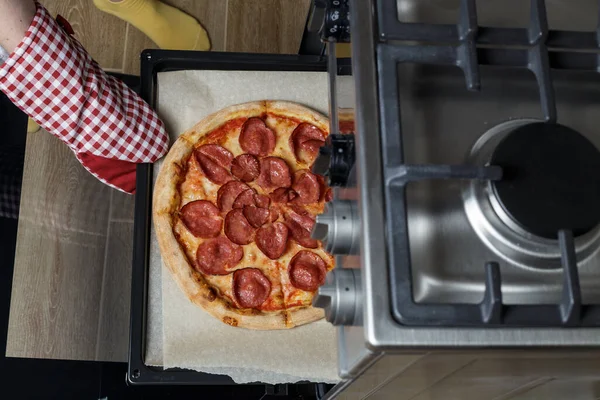 Kız pizzayı fırından çıkarıyor. Ev yapımı pepperoni pizza.