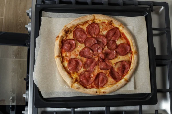 Fırında yeni pişmiş pizza ve kabartma kağıdı. Fırının üstünde pizzalı bir çarşaf var.