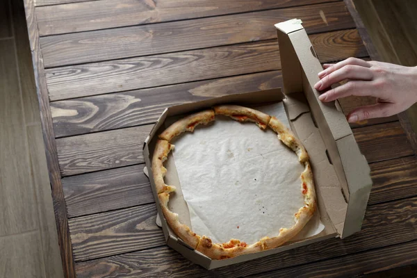 a woman's hand opens an empty pizza box with leftover food. Leftover pizza in a box.