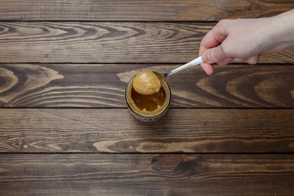 Kız kaşıktan fıstık ezmesi alıyor. Tahta bir masada kavanozda fıstık ezmesi.