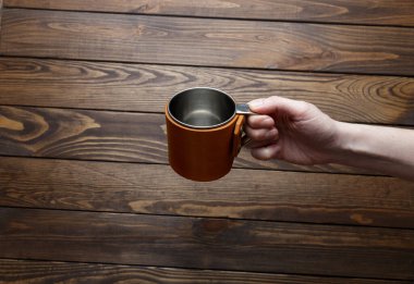 Kızın elinde bir kupa var. İzole edilmiş deri kollu paslanmaz çelik bardak. seyahat kupası ahşap arka planda.