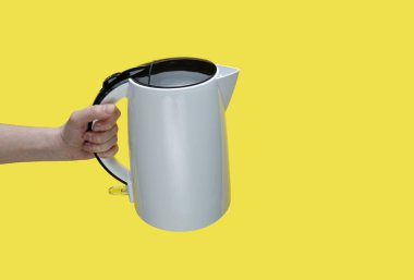 Sarı arka planda elektrikli su ısıtıcısı tutan kız..