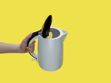 Sarı arka planda elektrikli su ısıtıcısı tutan kız..