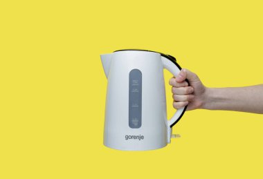 Zaporozhye Ukrayna - 8 Mayıs 2022: Sarı zemin üzerinde Gorenje elektrikli su ısıtıcısı tutan kadın.