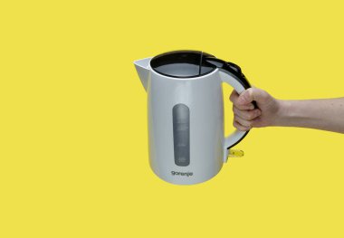 Sarı arka planda elektrikli su ısıtıcısı tutan kız..