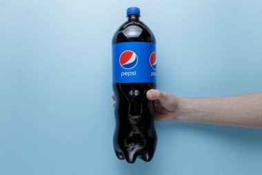Zaporozhye Ukrayna - 8 Mayıs 2022 Pepsi Cola şişesi 2L. Kadın eli mavi arka planda bir şişeyi tutuyor.