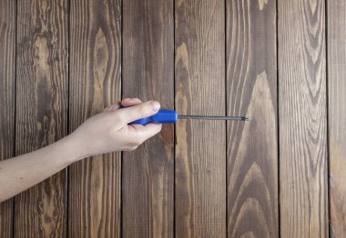 a girl holds a screwdriver in her hand next to a wooden background.