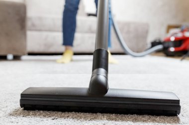 Ev temizliği konsepti. Bir kızın bacaklarının yakın plan fotoğrafı ve elektrikli süpürge fırçası. Kız evi temizliyor ve halıyı süpürüyor..