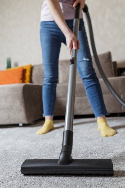 Ev temizliği konsepti. Bir kızın bacaklarının yakın plan fotoğrafı ve elektrikli süpürge fırçası. Kız evi temizliyor ve halıyı süpürüyor..