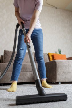 house cleaning concept. a close-up photo of a girl's legs and a vacuum cleaner brush. the girl cleans the house and vacuums the carpet.
