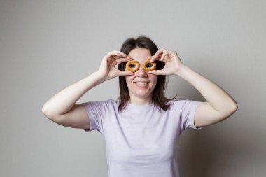 Neşeli bir kız gülümser ve gözünün önünde gözlük yerine iki simit tutar..