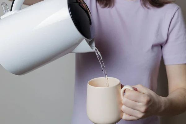 girl pours water from a kettle into a cup