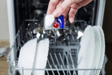 Kız bulaşık makinesine bir tablet yüklüyor. Kız bulaşık makinesinde bulaşık yıkıyor..