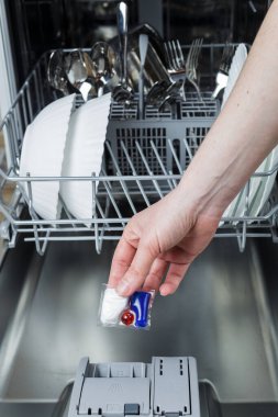 Kız bulaşık makinesine bir tablet yüklüyor. Kız bulaşık makinesinde bulaşık yıkıyor..