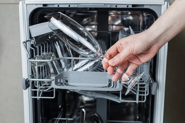 the girl checks the quality of the washed dishes after the dishwasher. girl holding a glass of wine on the background of the dishwasher