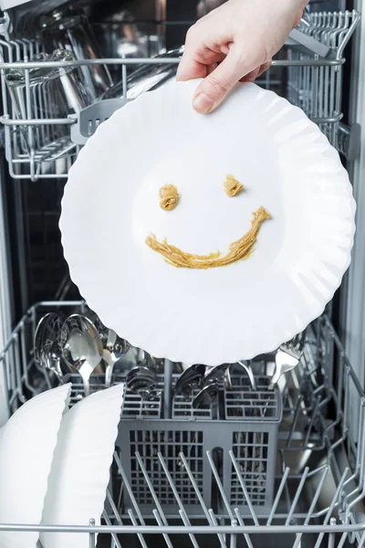 perfectly washed dishes in the dishwasher. hand holds a plate on which a smile is drawn