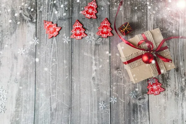 Jul presentförpackning och röd jul leksaker på en trä bakgrund med snöflingor och bländning. Royaltyfria Stockbilder