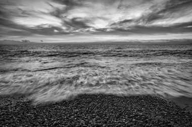 Okyanus Denizi 'nin Gün batımı. Dalgalar siyah ve beyaz resim biçiminde kıyıya vururken ayrıntılı bulutlu bir hava.