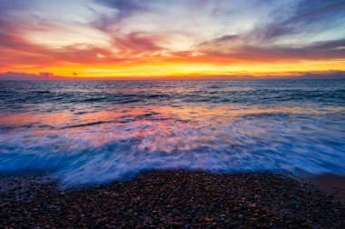Kum kıyısına dalgalar gibi dalgalanan renkli gökyüzü ile bir manzara okyanusu.