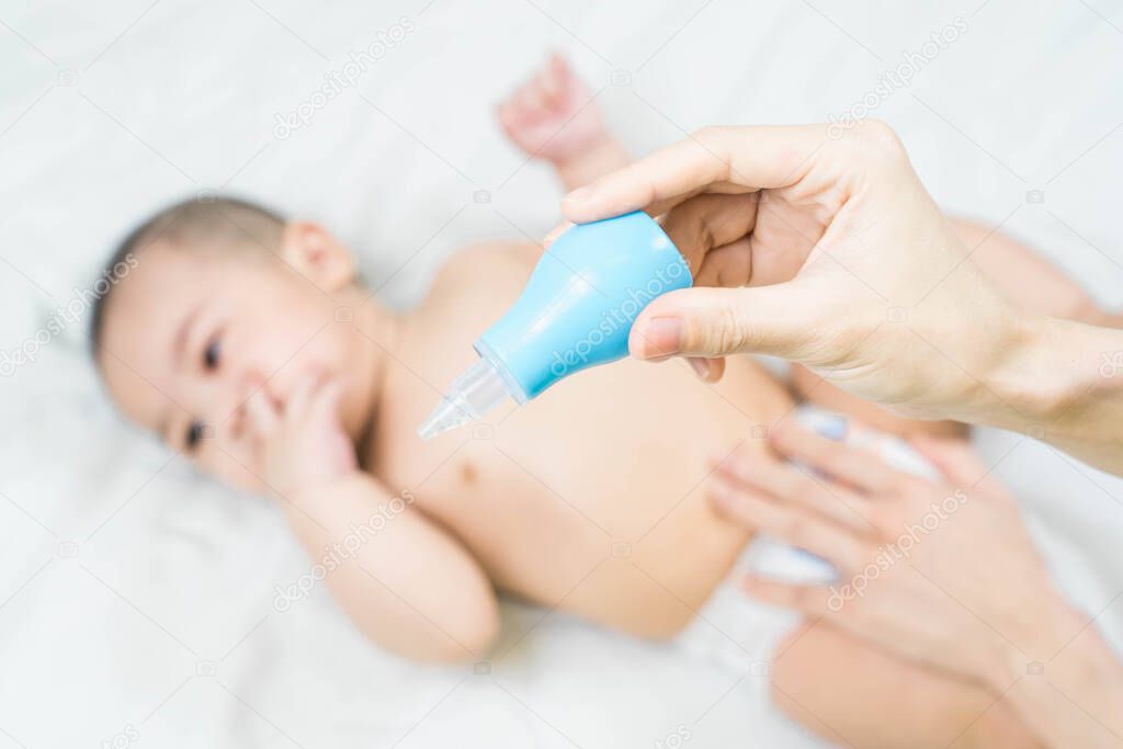 Selective focus Cute asian happy 5 months baby boy and mother's hand holding blue baby nasal aspirator or snot sucker. Baby Care Concept, cleaning wipe, pure, clean.