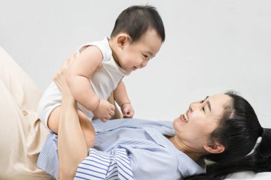 Selective focus Beautiful mom kissing on the cheek newborn with love and caring, Mother showing love to toddler with kiss on cheek.infant baby lying on bed with asian mom.