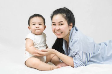 Happy young asian mother lying and holding adorable baby's hand with love and caring on the blanket at home, looking at the camera on white background
