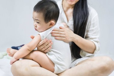 Selective focus on Mother's hand is belching for infant baby by stroking the back with a hand after breastfeeding on bed at home.