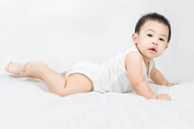 side view of cute asian baby boy is lying on bed on white blanket. Still unable to walk. Crawling only and looks at camera on a white background.Healthcare and family concept.