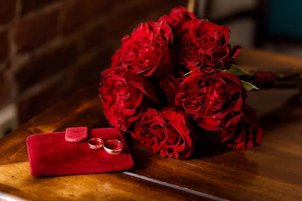 两只红白相间的结婚戒指 缀着一束红玫瑰的新娘花 图库照片