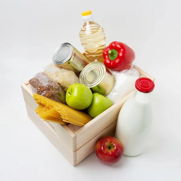 Pudełko z datkami. Jabłka, spaghetti, cukier, Crupes, olej słonecznikowy, pieprz bułgarski, konserwy, mleko w drewnianym pudełku na białym tle — Zdjęcie stockowe