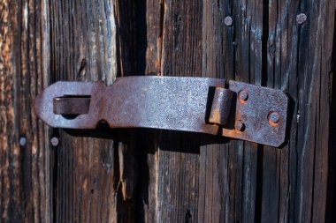 Ahşap kapıya asılı bir ahır kilidi için eski, paslı bir menteşe. Yan görüş. Yakın plan. Gün ışığı.