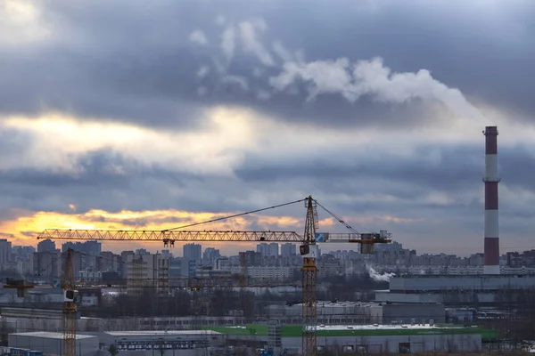 ロシアの喫煙パイプを持つ大都市の風景の郊外の家の上に太陽からの緑の線と冷たい秋の日の出 手前の煙管と2本の鶴 — ストック写真