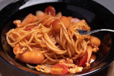 Domates soslu spagetti, siyah tabakta tavuk ve sosis. Düz yatıyordu.