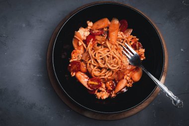 Domates soslu spagetti, siyah tabakta tavuk ve sosis. Düz yatıyordu.