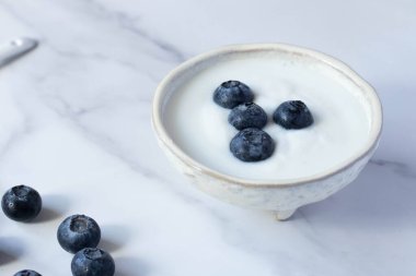 Beyaz fincanda mermer zemin üzerinde taze yaban mersinli yoğurt