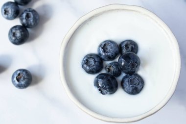 Beyaz fincanda mermer zemin üzerinde taze yaban mersinli yoğurt
