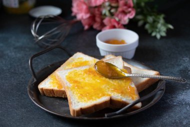 Ekmek, turuncu marmelatla kaplanmış siyah bir tepside..