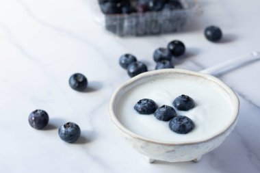 Beyaz fincanda mermer zemin üzerinde taze yaban mersinli yoğurt